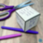 A completed story cube for the short story "The Gift of the Magi" sits on a desk with colored pens and a pair of scissors.