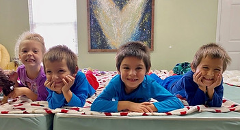Four children are laying on their stomachs next to each other smiling and laughing
