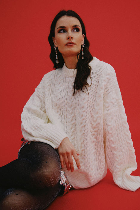 Woman wearing oversized white cable knit sweater and long drop earrings.