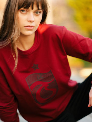 Woman models deep red sweatshirt with dark graphic design outdoors.