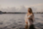 A pregnant woman standing waist deep in water at sunset, wearing a beautiful white dress