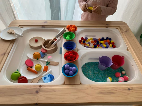 Bebê pegando objetos pequenos em mesa sensorial desenvolvendo coordenação motora fina