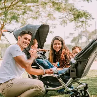 Pais passeando com dois bebês em carrinho duplo