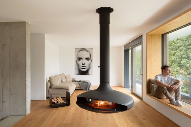 Wohnbereich eines modernen Ferienhauses mit freihängendem Kamin und bodentiefen Fenstern