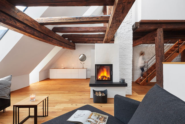 Wohnbereich eines renovierten Altbau-Ferienhauses mit sichtbaren Holzbalken und Kamin