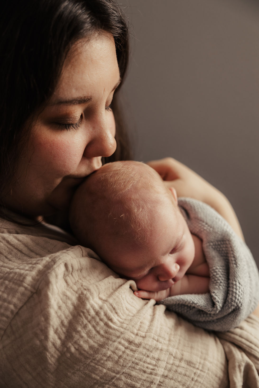 Mutter hält und küsst ihr Neugeborenes – Familienshooting zu Hause bei natürlichem Licht
