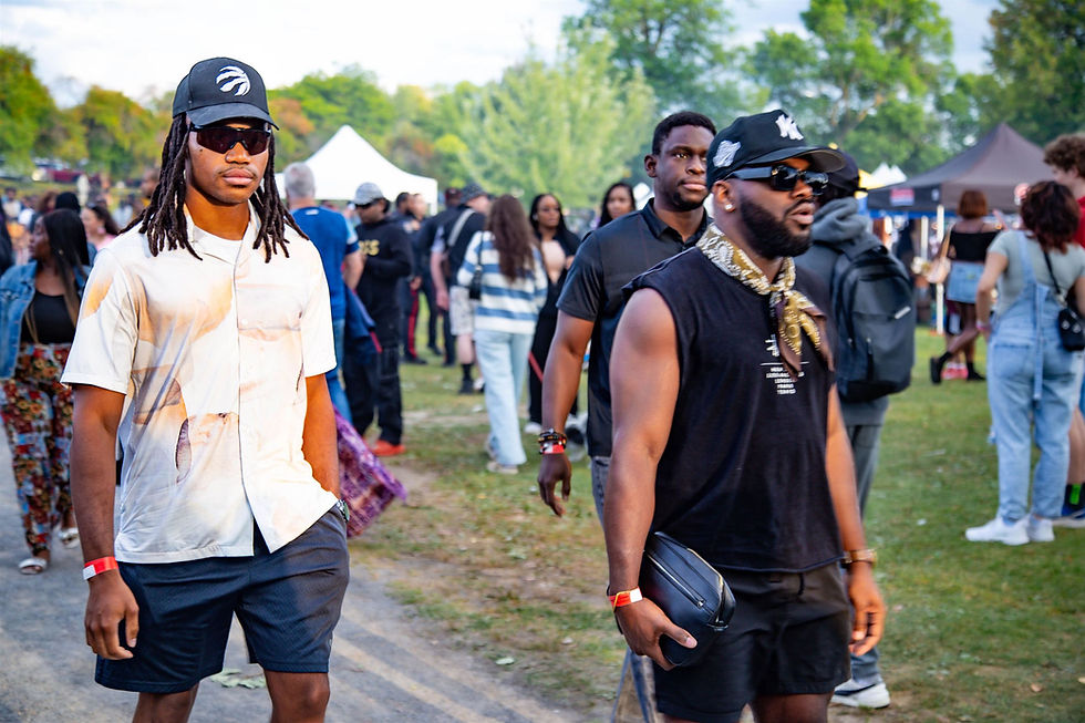 Outdoor festival (Arofest Ottawa) scene with people walking. Two men in shorts and hats are in the foreground. Tents and trees in the background. Casual mood.