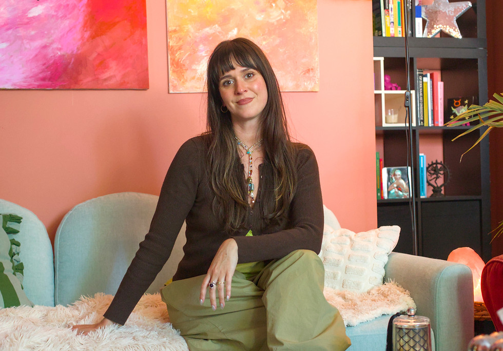 a woman dressed in earth tones, smiling and sitting on a mint green couch in a terracotta painted room in front of two paintings
