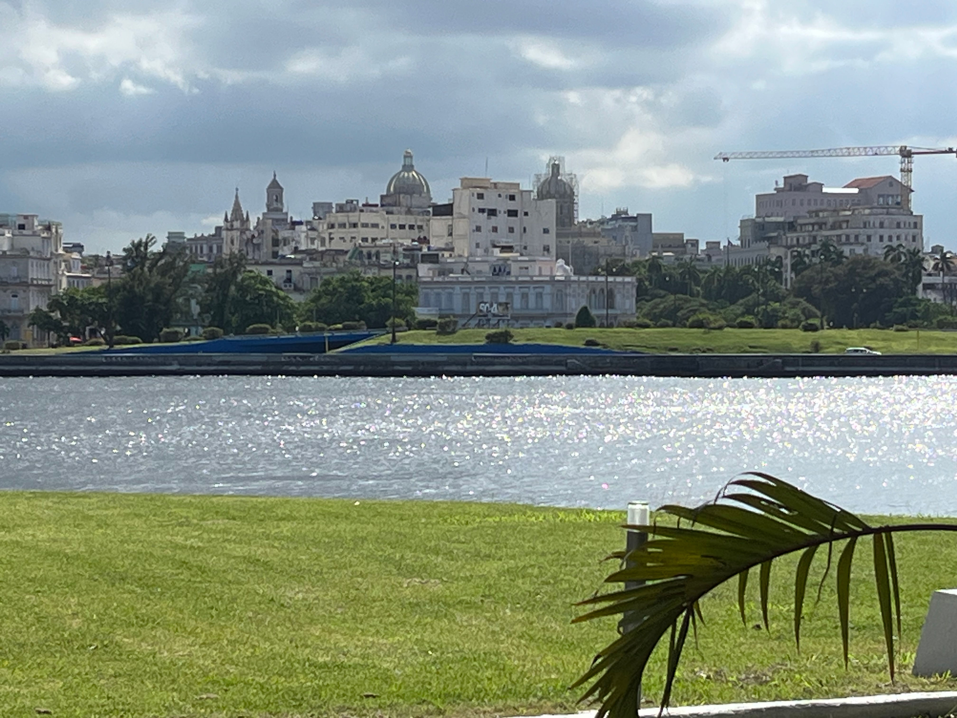 Havana skyline across sparkling water from green riverbank, cloudy sky.