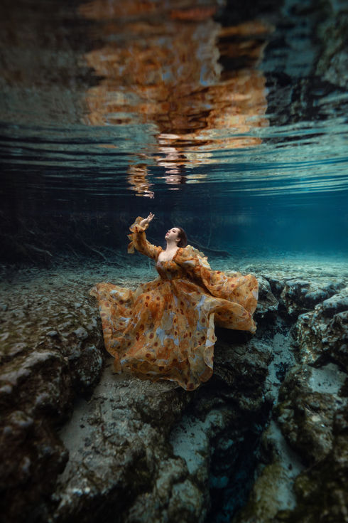 Kalynn is in a golden sunflower gown inspired by Van Gogh’s famous artwork. She sits on a rocky outcropping above a deep, underwater crevice, and reaches up towards the rippling surface.
