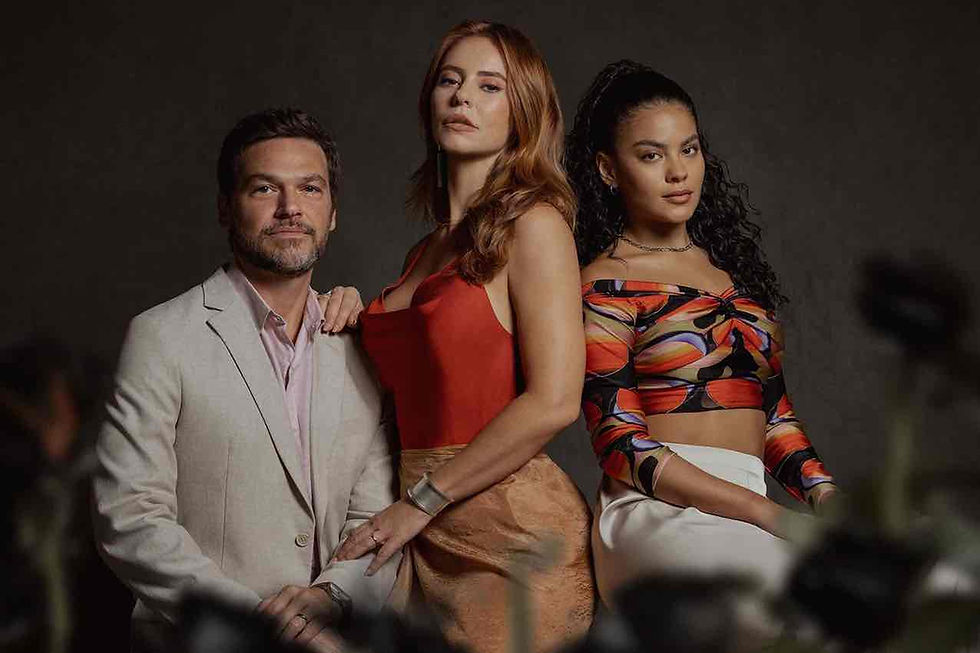 Fotografia promocional do thriller da Netflix "A Estranha na Cama", com os atores Emilio Dantas, Paolla Oliveira e Bella Campos posando em estúdio. Emilio usa blazer claro; Paolla, no centro, veste top vermelho; e Bella usa top colorido.Crédito: Marcos Serra Lima/Netflix