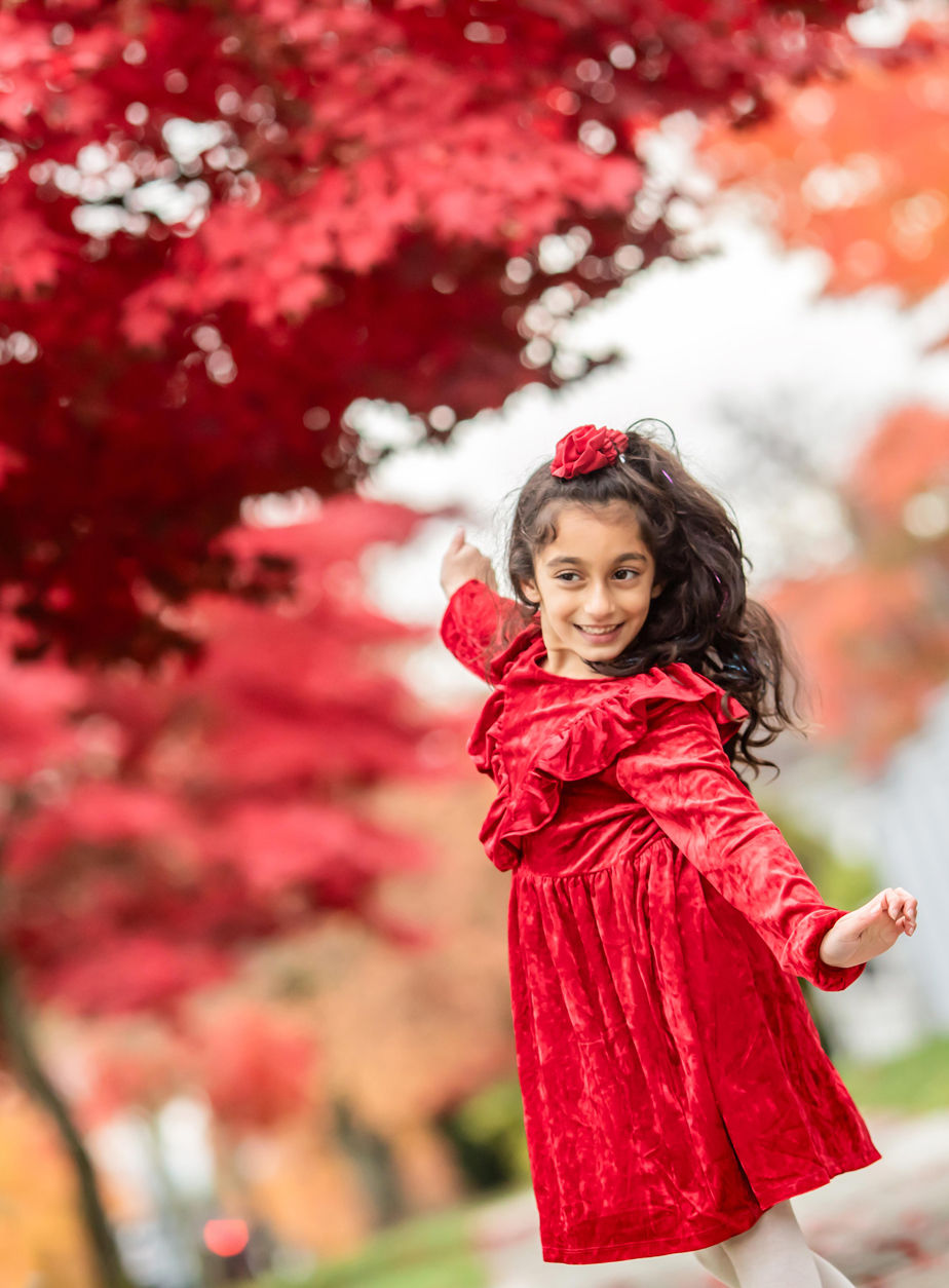 young girl in a red dress dances in the leaves