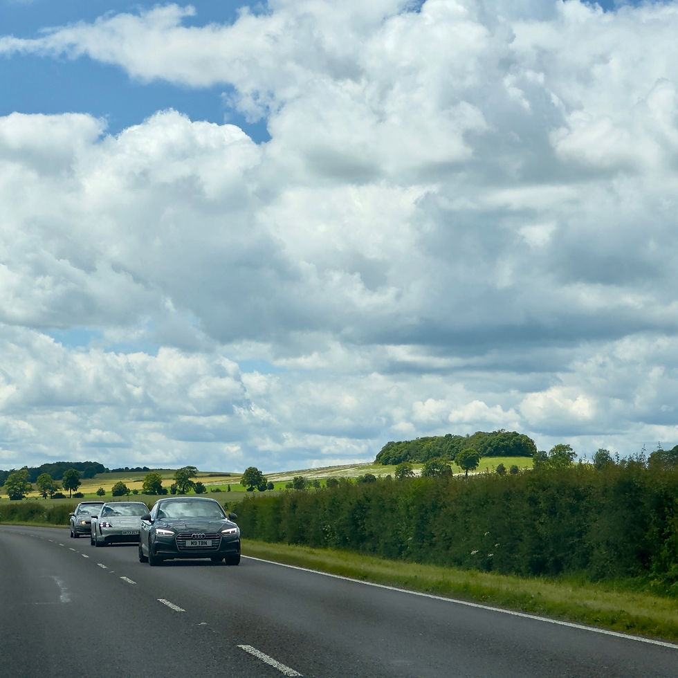 three cars driving down a country road with rolling green hills in the background.