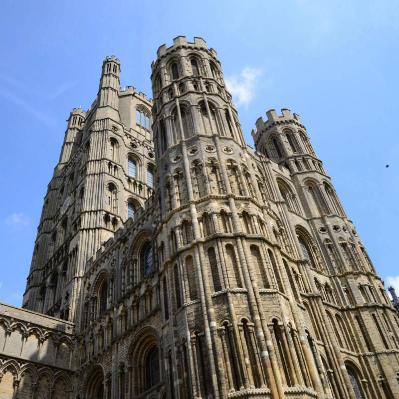 Low-angle view of Ely Cathedral towers set against a vibrant blue sky in England.