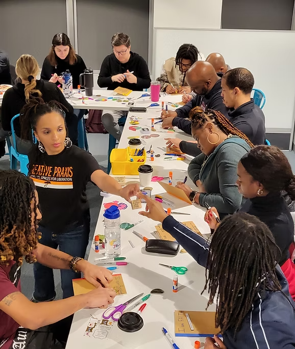 A group of adults seated around a table participating in an arts-based professional development session.