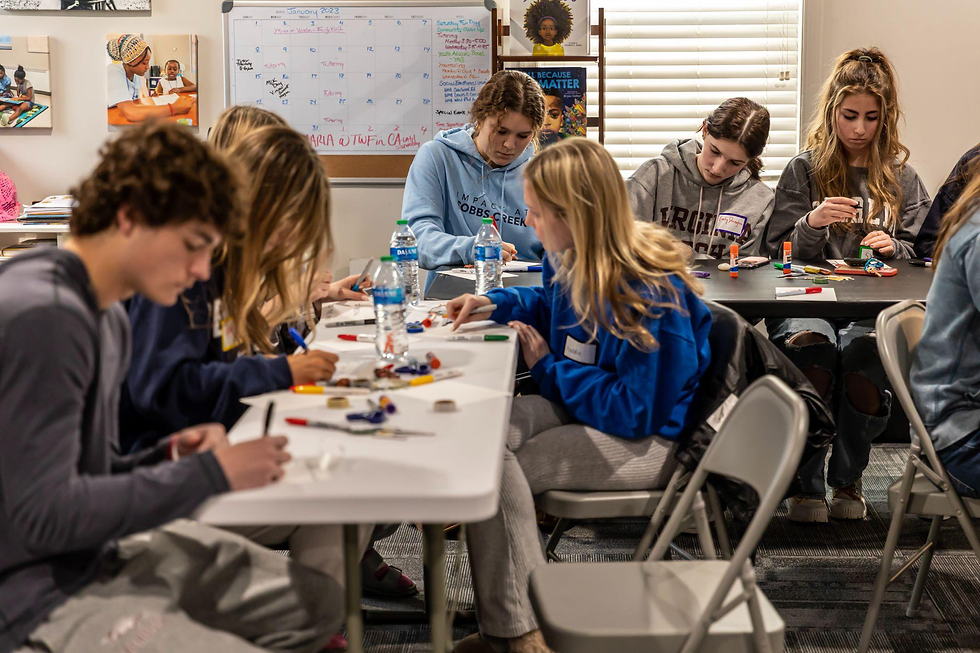 Students in a classroom setting working quietly on art projects with supplies spread across their desks