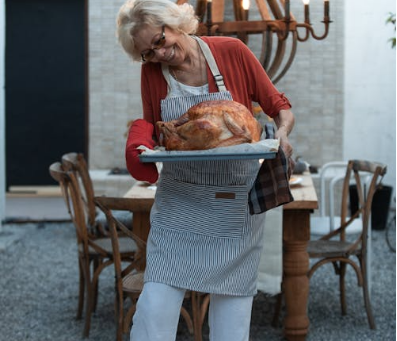 A woman holds a turkey at her Thanksgiving table with an outdoor chandelier.