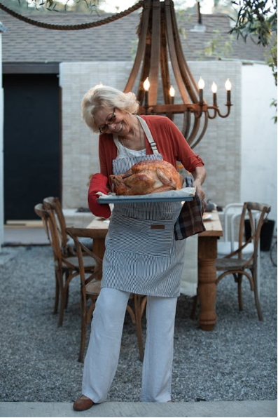 A woman holds a turkey at her Thanksgiving table with an outdoor chandelier.