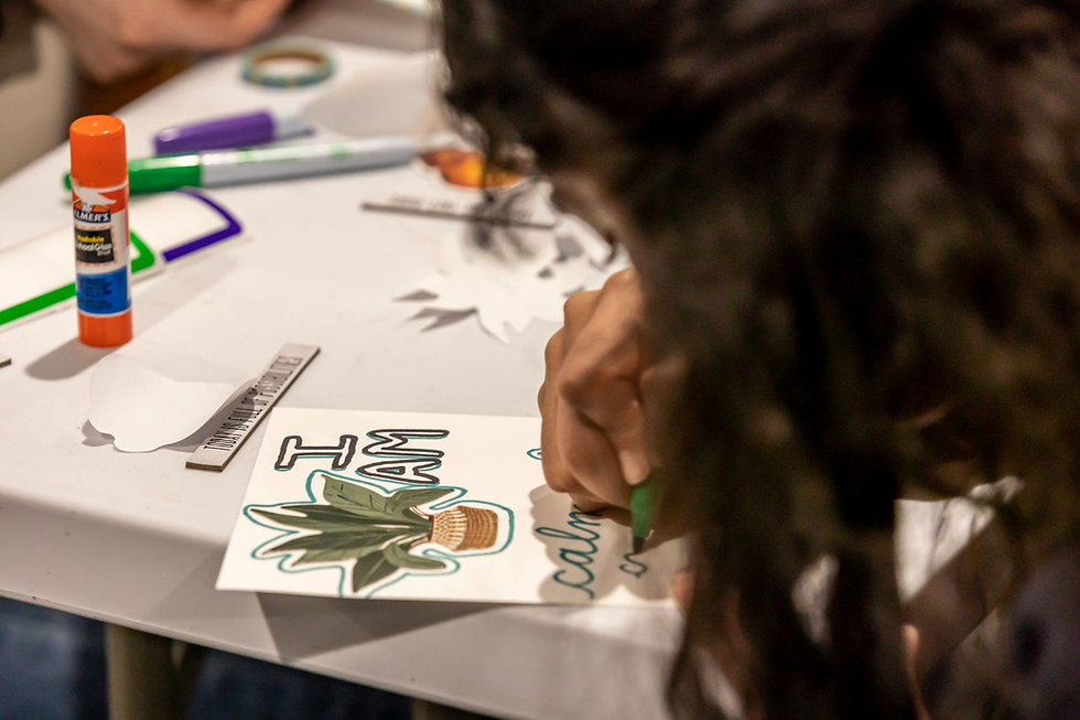 Child using a marker to color in an art sheet with glue sticks and supplies nearby