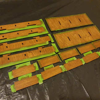 Woodstained components from the Laserox Hogwarts Battle Organizer laid out on some black plastic with slotting edge pieces covered  with protective green paper