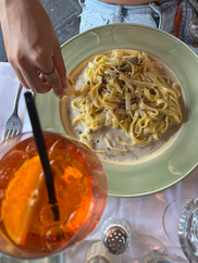 hand dipping bread in sauce from spaghetti, aperol spritz drink in the corner of the photo 