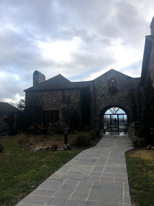 Stoned building, on the right a tiled pathway leads to an arched glass entrance