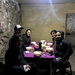 Hikers around a table ready for dinner sitting under a small hut
