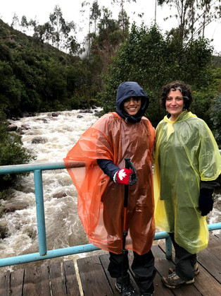 Two women in ponchos smiling in front of a stream