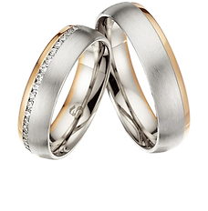 Zwei silberfarbene Trauringe mit goldfarbenen Details; ein Ring ist mit kleinen Steinen besetzt.
