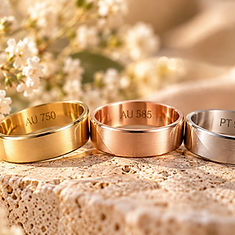 Drei Ringe in Gelbgold, Roségold und silberfarbenem Metall auf hellem Stein