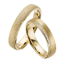Zwei goldfarbene Trauringe mit strukturierter Oberfläche; ein Ring ist mit kleinen Steinen besetzt.