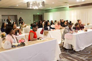 Conference with guests seated at long tables with white coverings and petite centerpieces