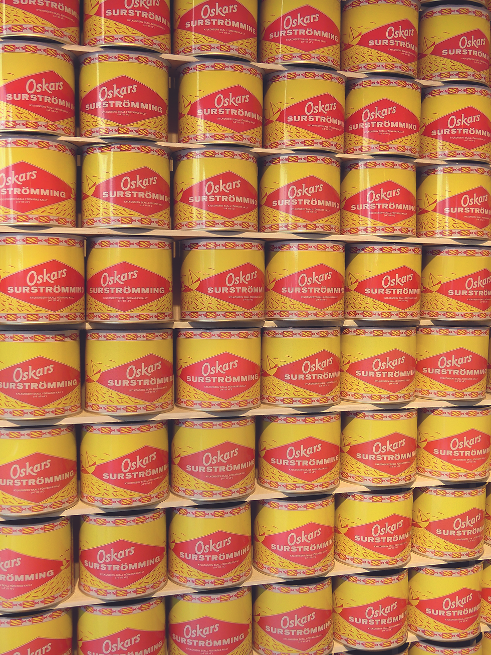 Gelbe und rote Dosen von "Oskars Surströmming" sind in einem Regal gestapelt. Die Dosen zeigen ein fischförmiges Muster.