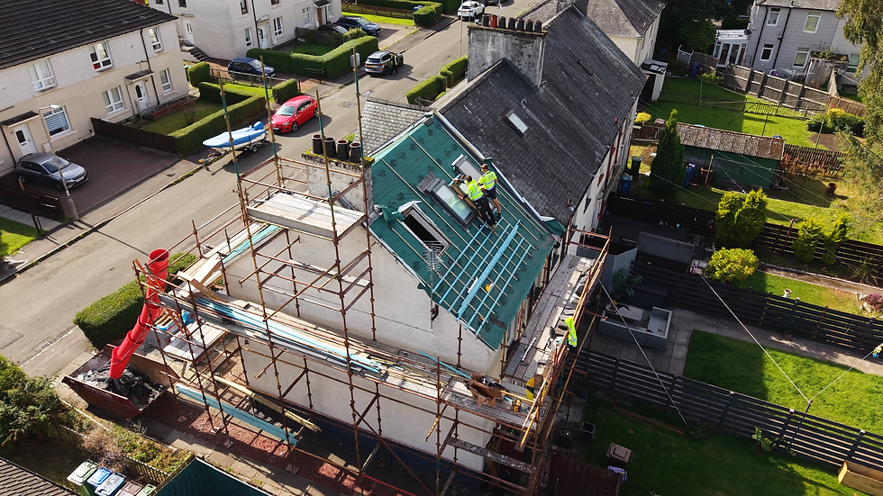 Workers on a roof installing green tarp with scaffolding surrounding a house.