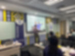 Facilitator standing at the front of a training room, presenting slides on a projector screen to par