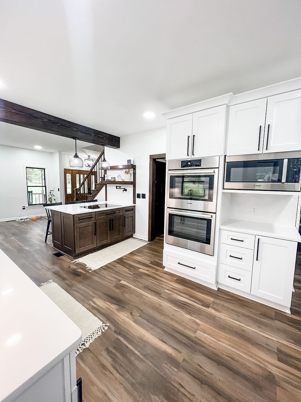Kitchen renovation showing hardwood floors, white cabinetry, stainless steel double oven, and dark wood island. Kitchen is open to the left to rest of house.