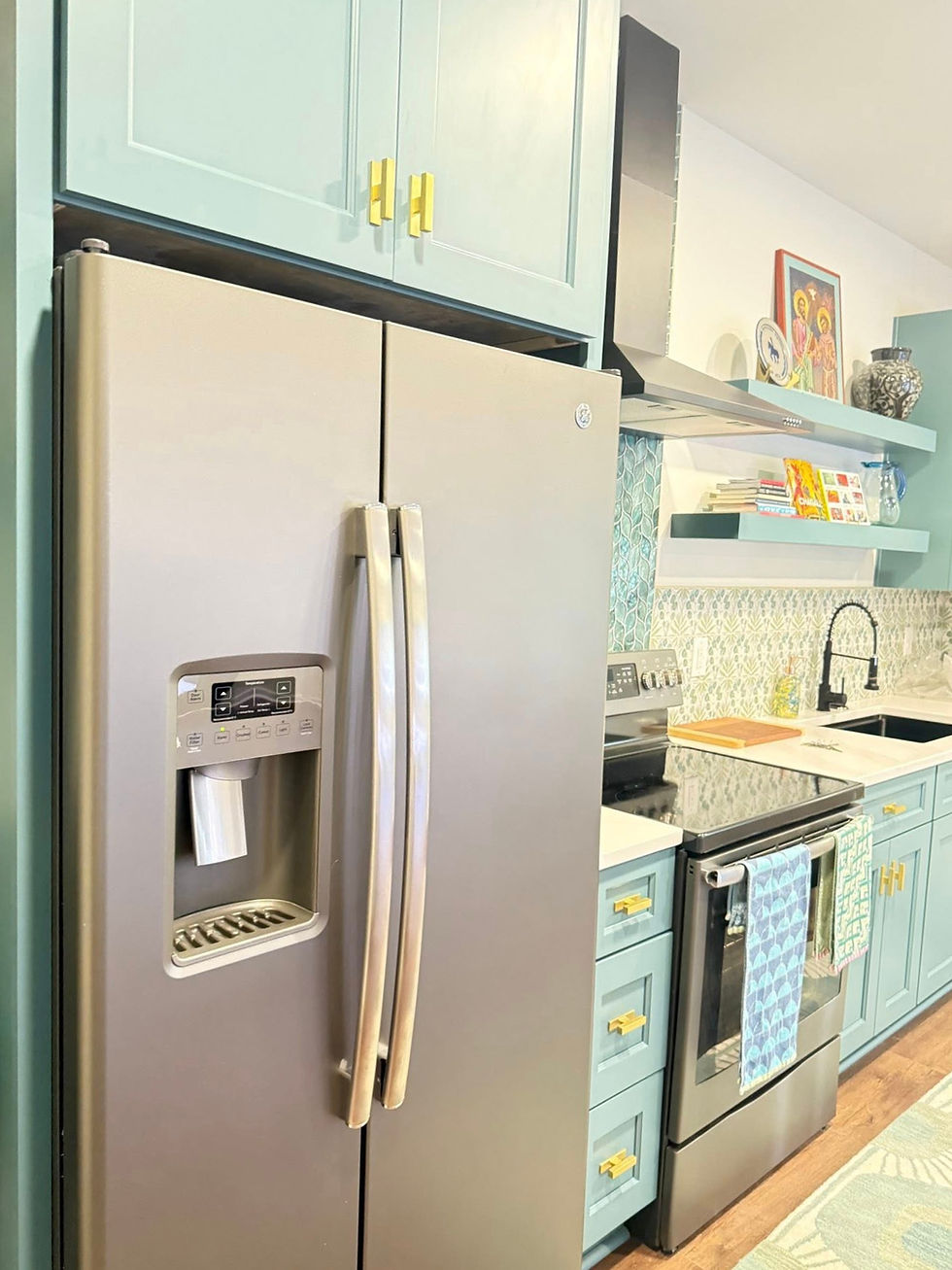 Modern kitchen with a stainless steel fridge, pastel blue cabinets, and a stove. Shelves with books, art, and decor add color and charm.