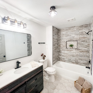 renovated bathroom showing hex tile flooring, natural gray tiled bathtub walls, and white sink and counter