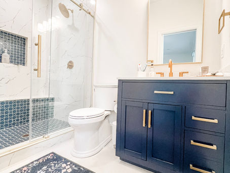 home renovation near Cornelius, NC featuring renovated bathroom with white walls, white tile flooring, marble shower surround, blue decorative accents, and dark blue vanity.