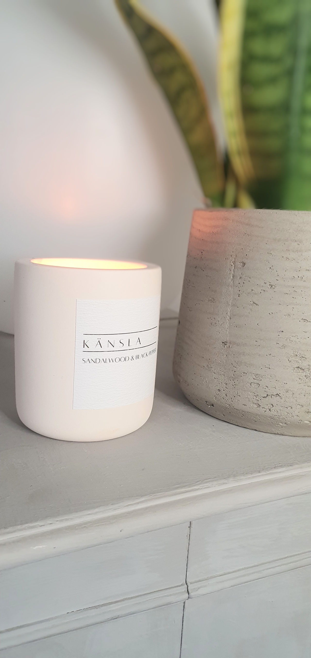 A warmly lit candle in a scent of sandalwood and black pepper from Känsla