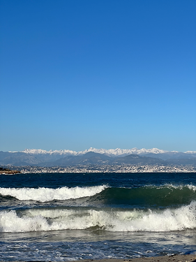 French Riviera, picture of crashing waves with snowy mountain caps in the background.