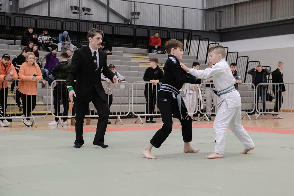 2 boys compete in a Brazilian Jiu-Jitsu match on the mats as spectators watch