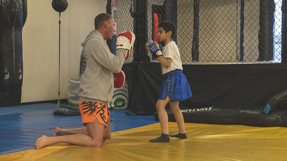 A young boy takes part in Muay Thai next to an MMA cage