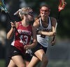 Two young female lacrosse players in action, one in red, the other in white, on a field.