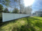 A white wooden fence stretches across a grassy field under a clear blue sky.