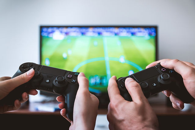 Two PlayStation controllers held in front of a TV screen.