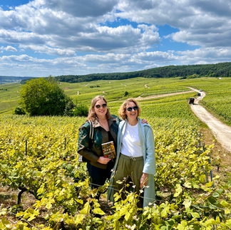 Bryn and Melanie stand in a vineyard under a bright blue sky