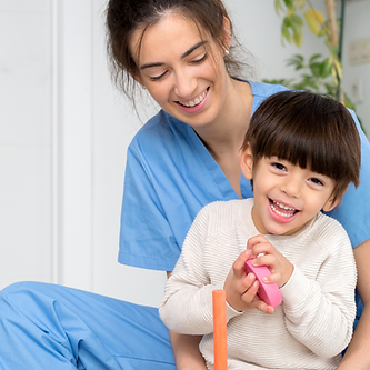 A young woman in scrubs holds a smiling young boy with CP