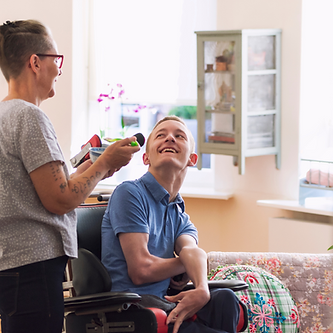 A young man in a wheelchair smiles up at a woman in a grey shirt