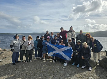 A group of women standing in front of a body of water holding a Scotland flag.